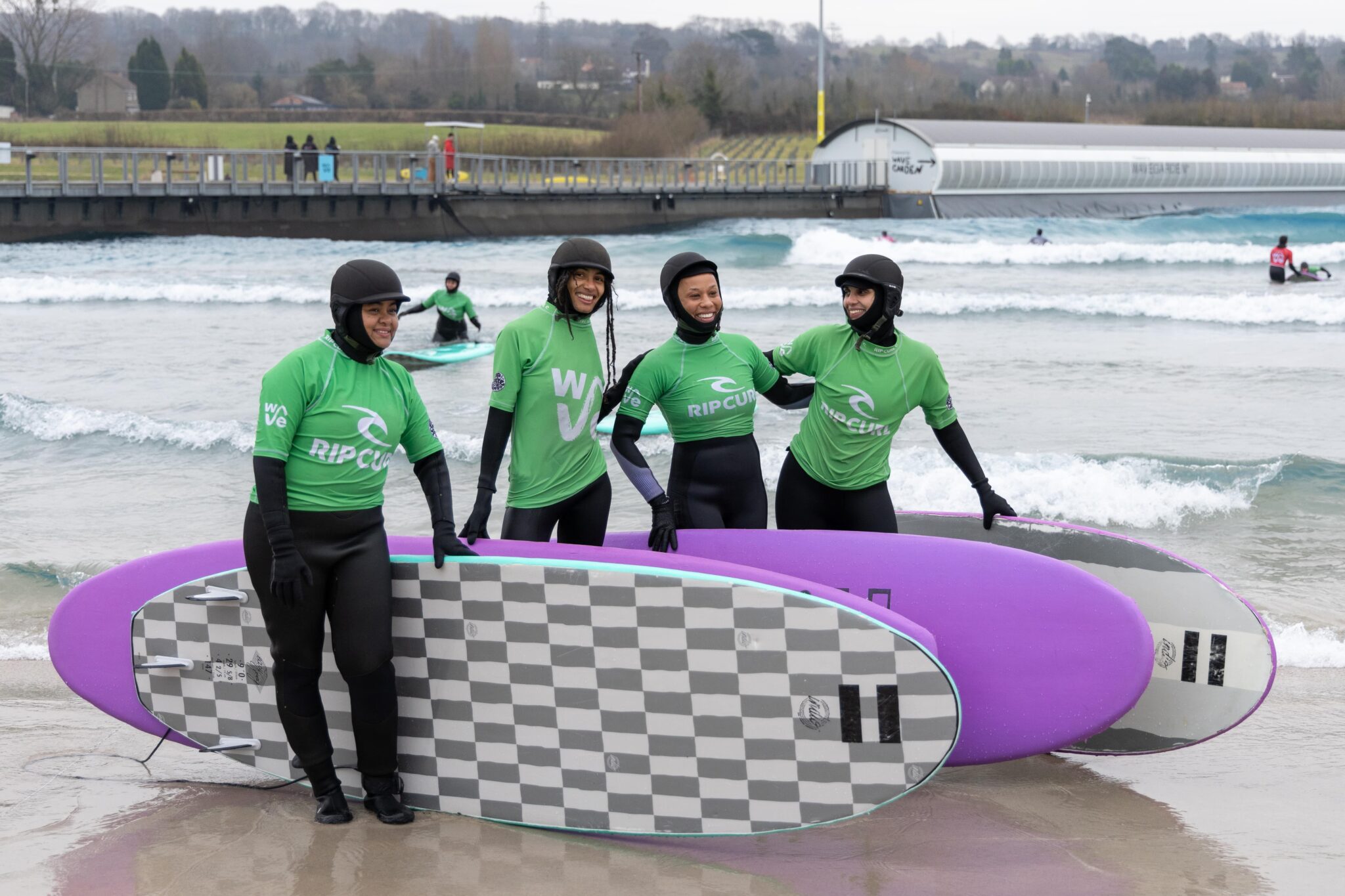 A woman smiles and waves while surfing in an Improver session at The Wave Bristol.