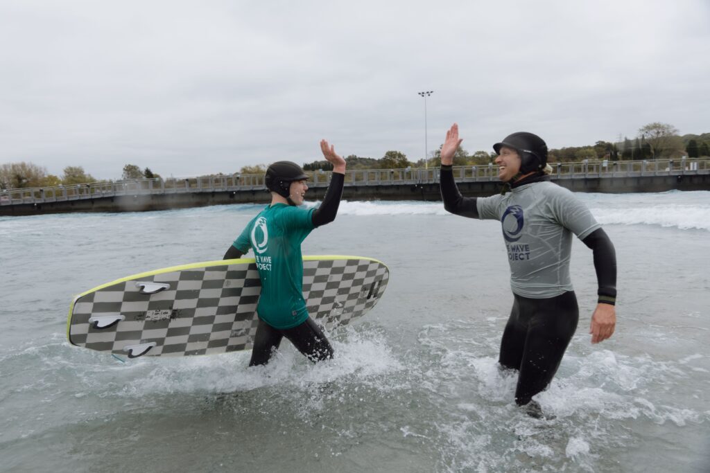 Two surfers from The Wave Project hi-five at The Wave Bristol.