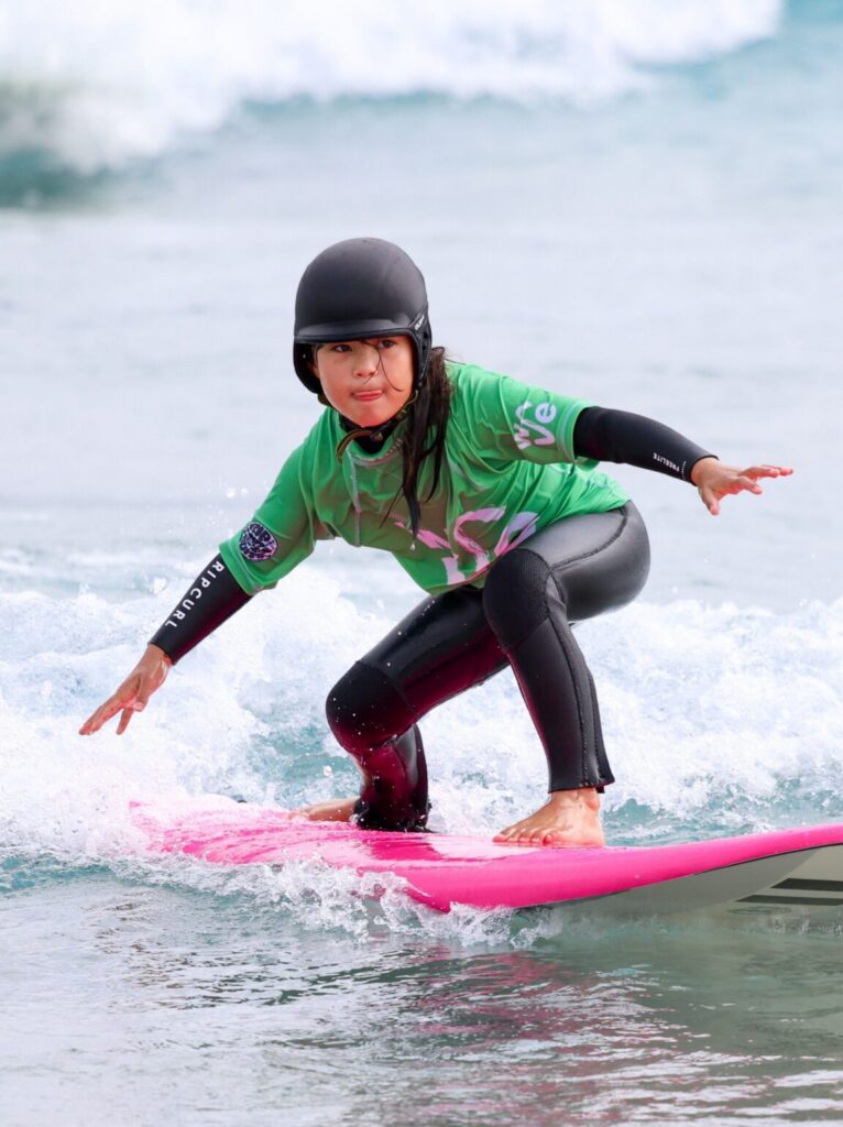 A young girl surfs a beginner wave at The Wave Bristol.
