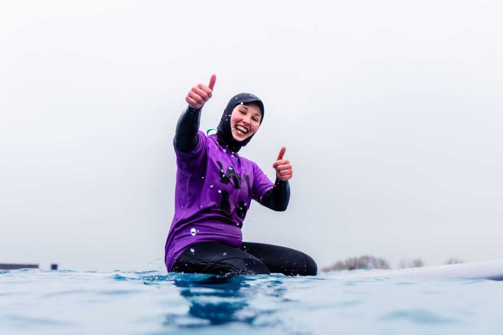 A female surfers poses and smiles for the camera while sitting on her board at The Wave Bristol.