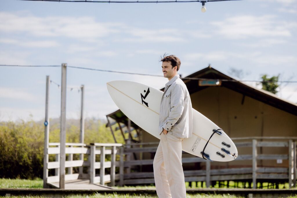 A surfer walks with his surfboard from The Camp to The Wave