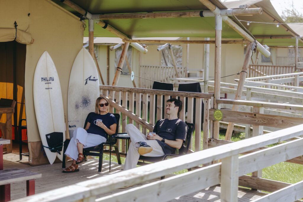 A man and woman sit on the Safari Tent balcony outside The Camp
