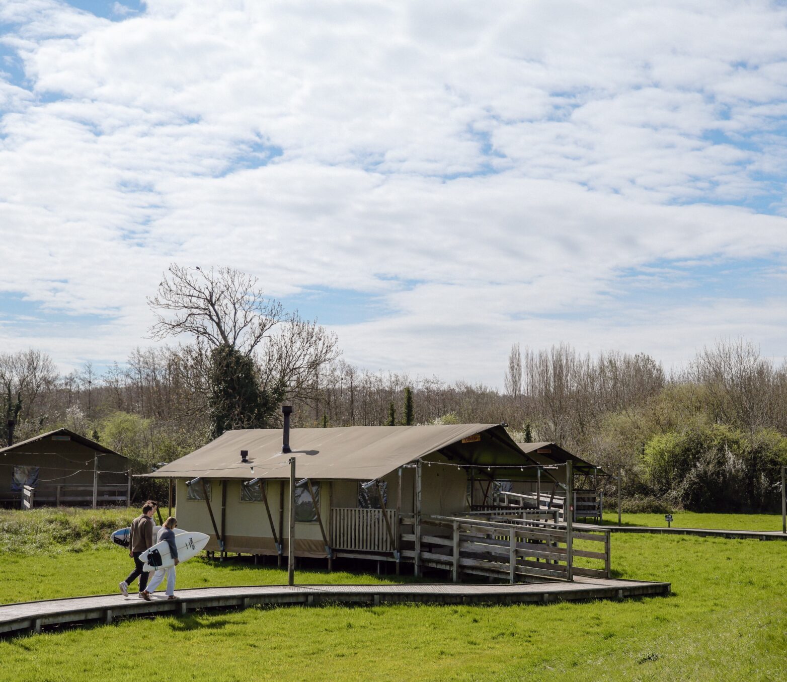 surfers walking alongside safari tent at the camp at the wave