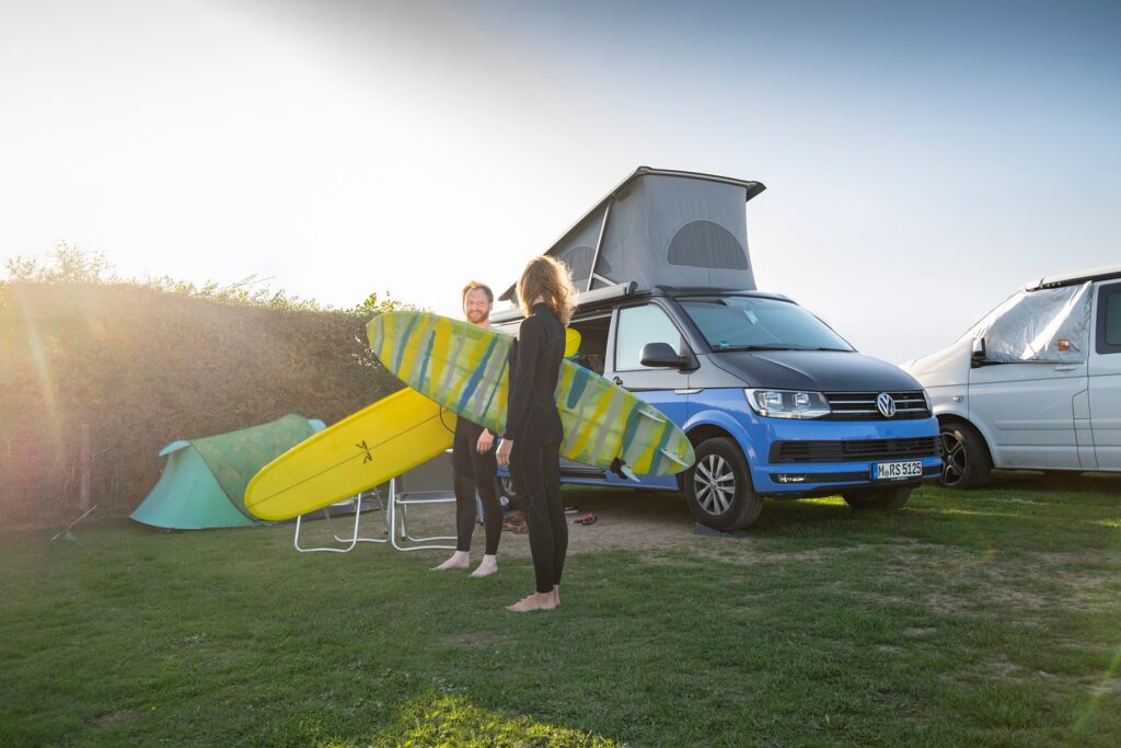 Couple with surfboards by campervan and tent